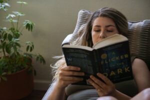 Дівчина зосереджено читає психологічний трилер, напівлежачи в кріслі. Атмосфера затишного читання та огляд на Фріда Макфадден книги на сайті Prime Feminine.